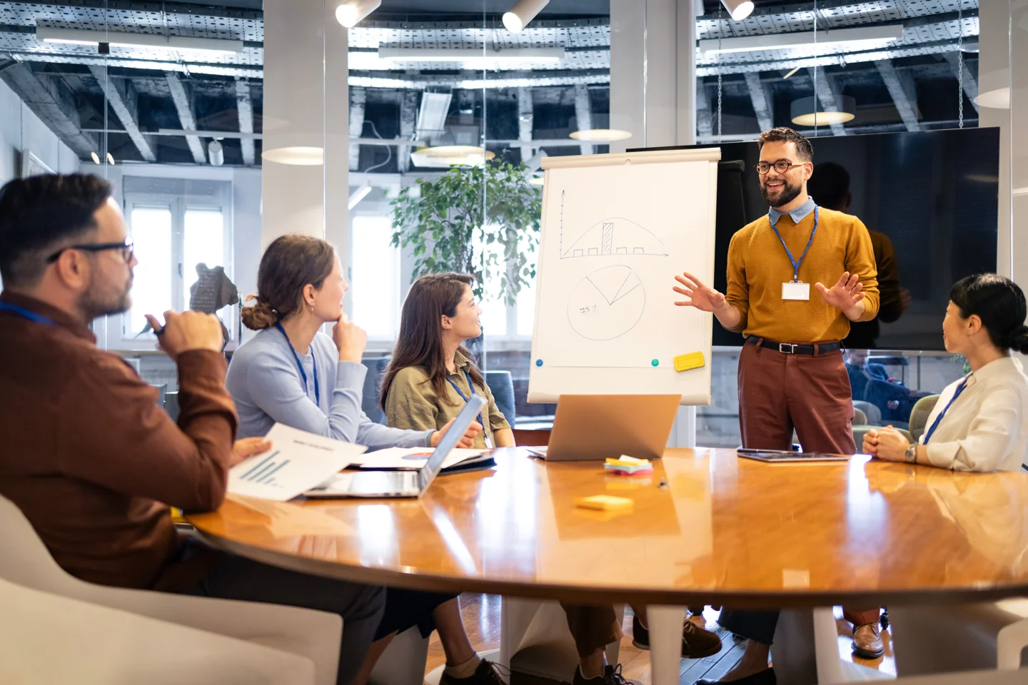 Arbeitssitzung an einem Besprechungstisch, ein Teilnehmer präsentiert am Flipchart